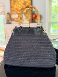 Black woven handbag with bamboo handle in a blurred indoor setting