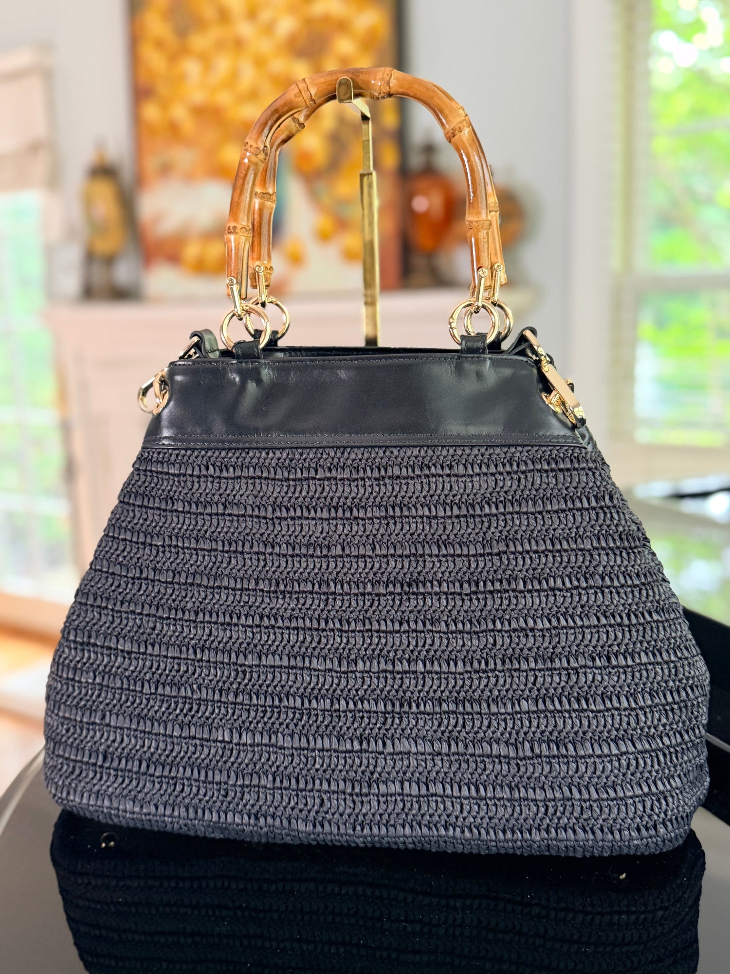 Black woven handbag with bamboo handle in a blurred indoor setting