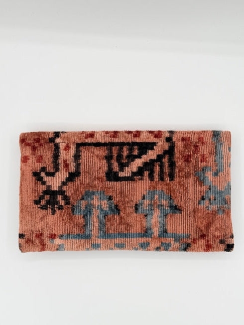 A folded vintage-style rug with a distressed terracotta orange base, featuring black and muted blue geometric and stylized motifs, displayed against a plain white background.