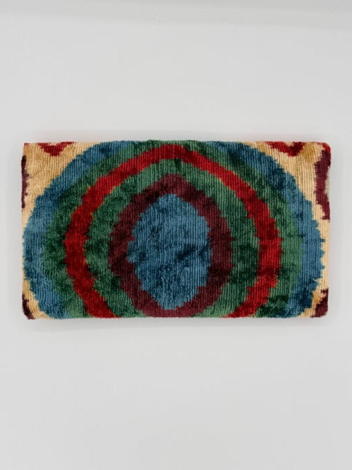 A rectangular woven rug with concentric circular patterns in blue, green, red, and beige, displayed against a plain light gray background.