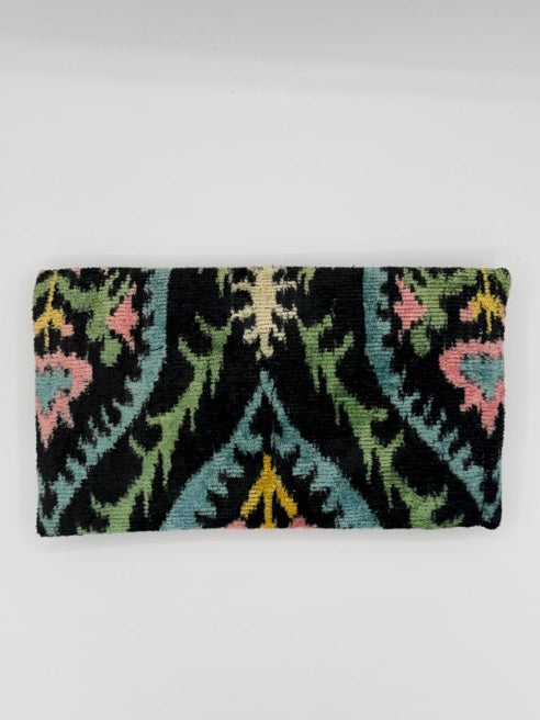 A rectangular woven textile with a black base and multicolored abstract floral and leaf patterns in pink, green, blue, yellow, and cream, photographed against a plain light background.