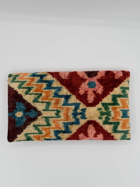 A vintage kilim rug with a geometric diamond pattern in red, orange, green, and blue on a cream background, displayed against a plain light gray wall.