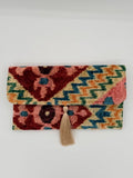 A small woven pouch or notebook cover with a geometric multicolor pattern and a beige tassel closure, photographed against a plain light background.