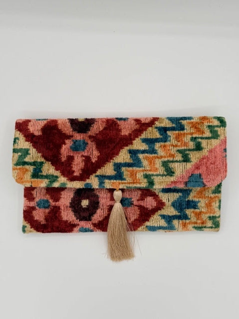 A small woven pouch or notebook cover with a geometric multicolor pattern and a beige tassel closure, photographed against a plain light background.