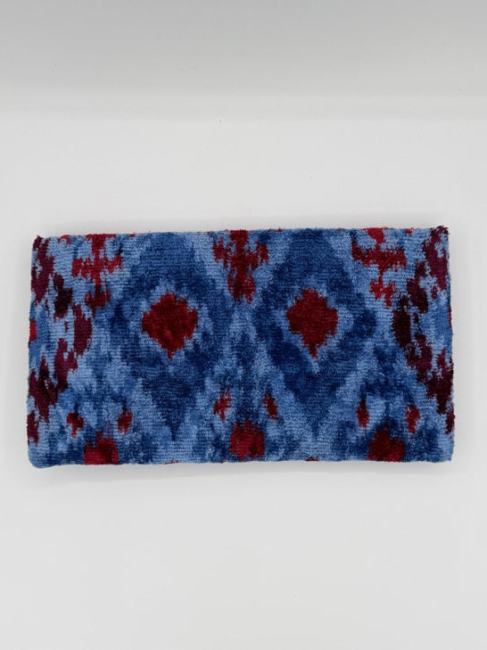A rectangular woven textile, likely a towel or blanket, featuring a blue and red ikat pattern, displayed against a plain light gray background.