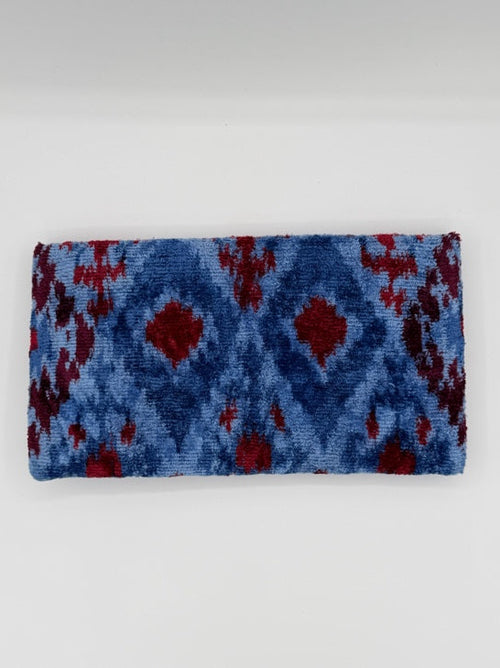 A rectangular woven textile, likely a towel or blanket, featuring a blue and red ikat pattern, displayed against a plain light gray background.