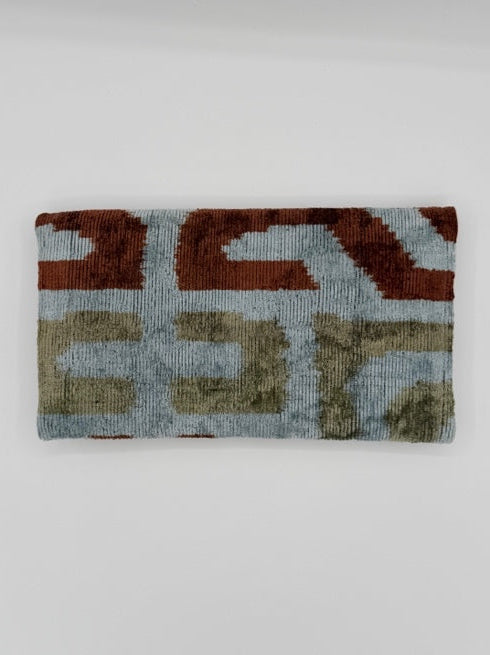 A rectangular woven clutch with an abstract geometric pattern in rust red, beige, and light blue-gray, shown against a plain light gray background.