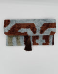 A folded woven textile with an abstract ikat-style pattern in brown, light blue-gray, and beige, featuring a dark brown tassel on the side, photographed against a plain light gray background.