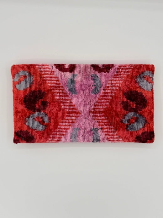 A rectangular woven textile with a red and pink geometric pattern and gray accents, displayed flat against a light gray background.