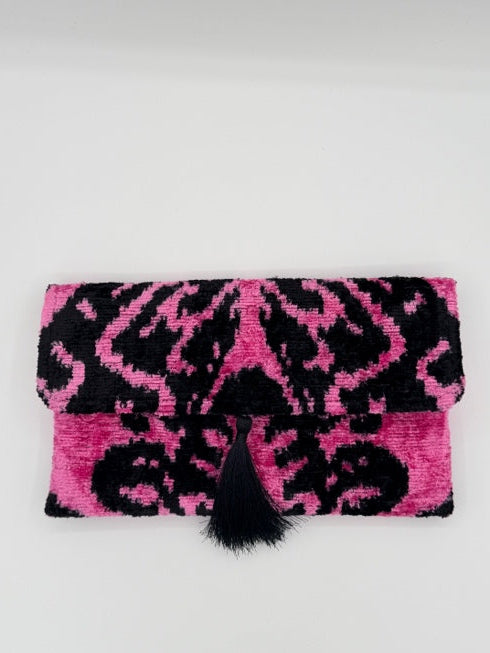A pink and black patterned fabric pouch or sleeve with a black pom-pom closure, photographed on a plain light background.
