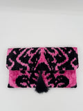 A pink and black patterned fabric pouch or sleeve with a black pom-pom closure, photographed on a plain light background.