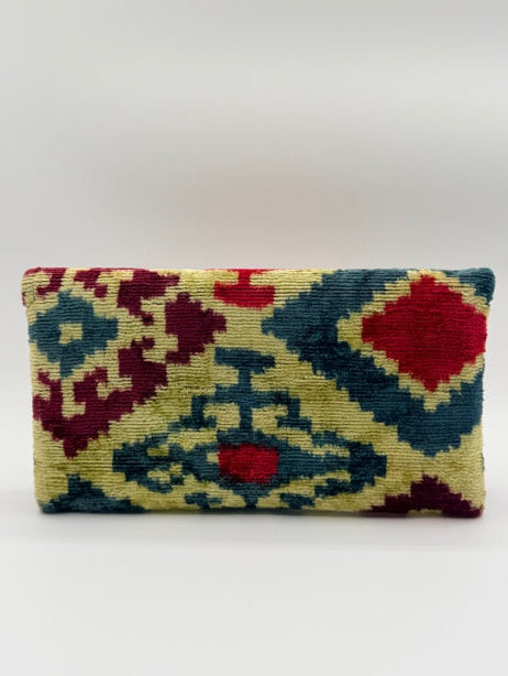 A rectangular woven textile with a geometric ikat-style pattern in red, navy blue, and beige, shown hanging against a plain light gray wall.