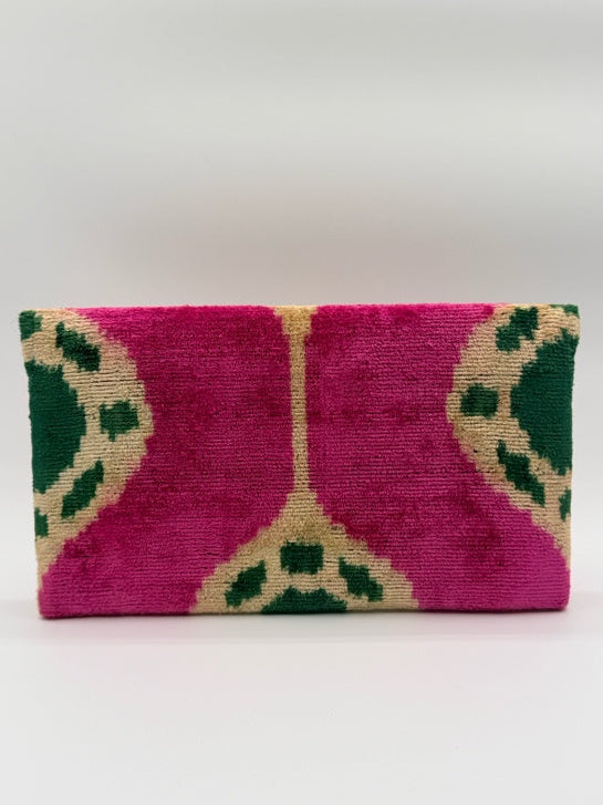 A rectangular woven textile clutch, featuring a vibrant magenta pink background with a geometric pattern in dark green and beige, shown against a plain white background.