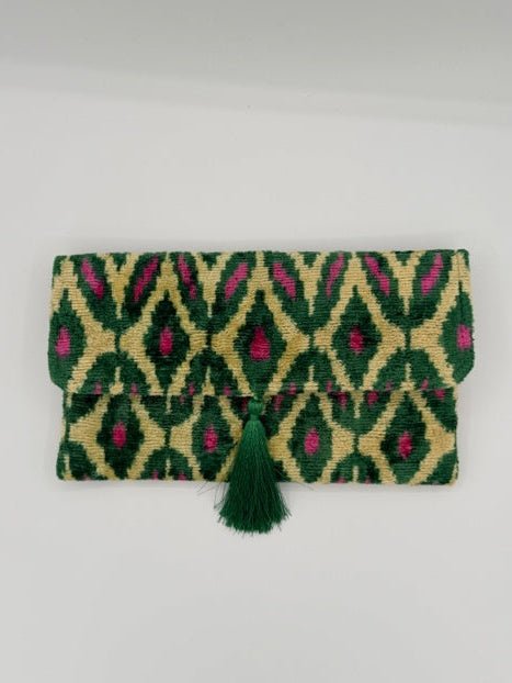 A folded woven textile pouch or notebook cover with a green and beige geometric diamond pattern and a dark green tassel, shown on a plain light background.